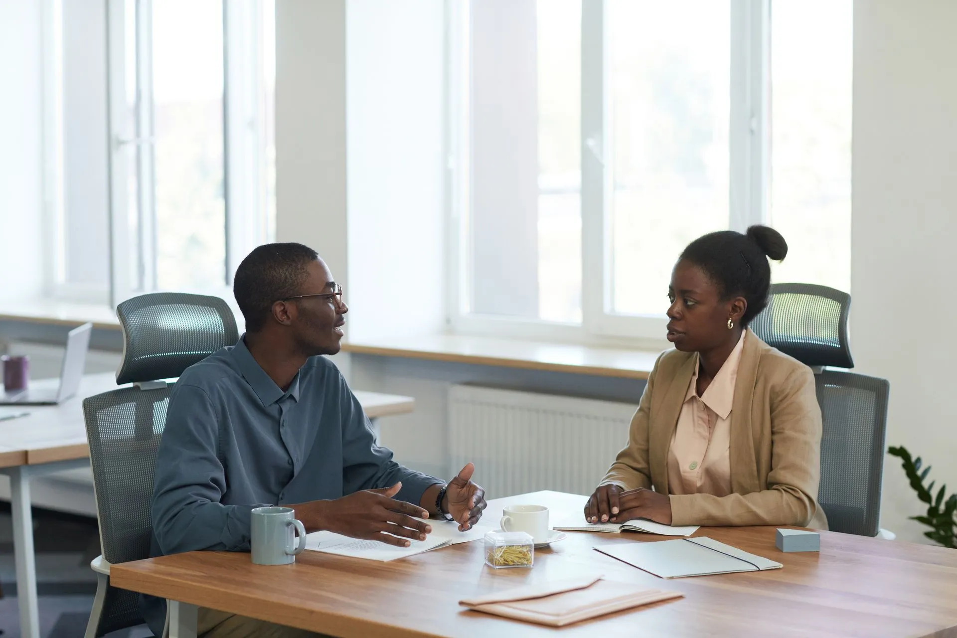 Man explaining a point to a woman across an office desk in a one-on-one meeting