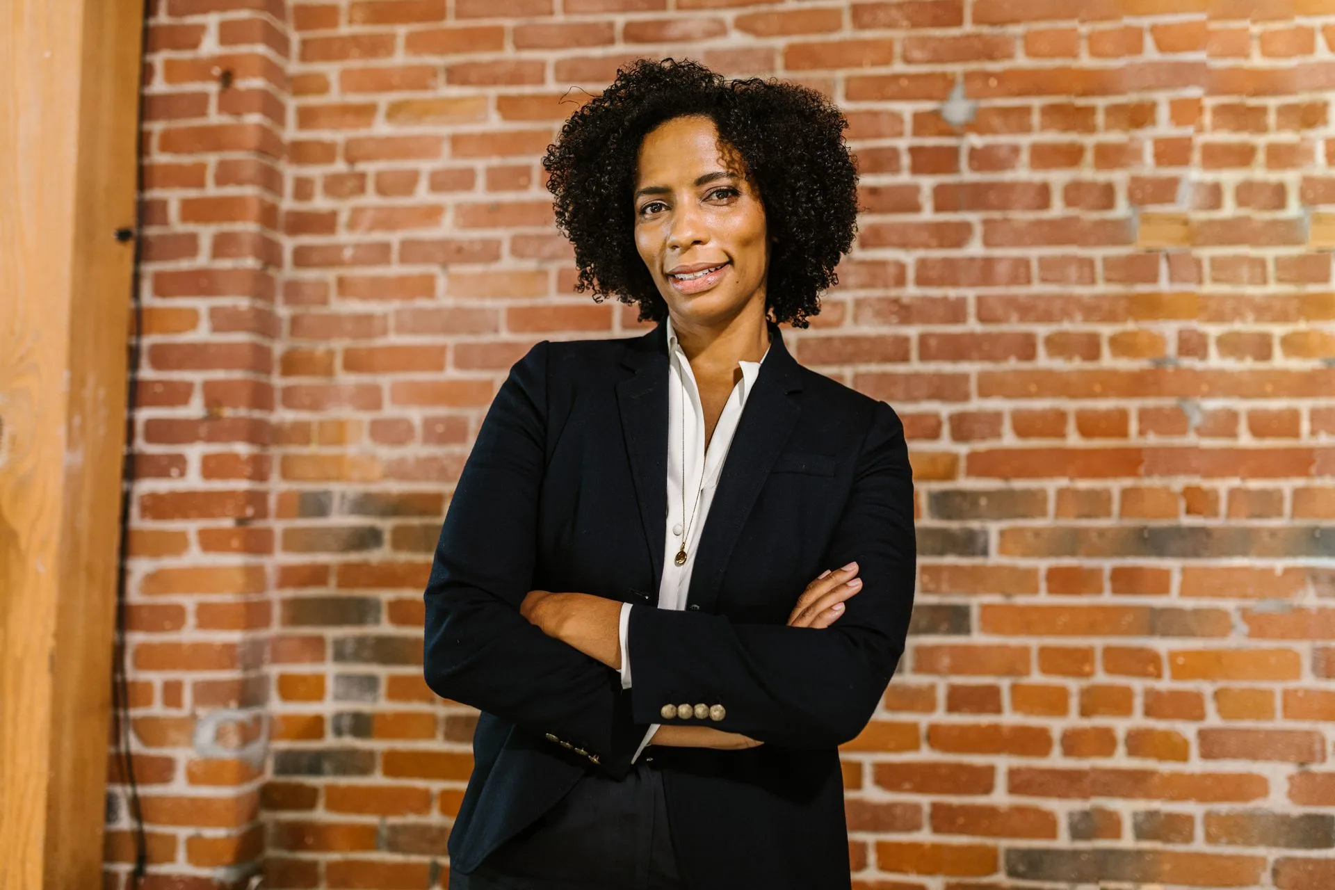 Confident female leader with arms crossed in front of a brick wall