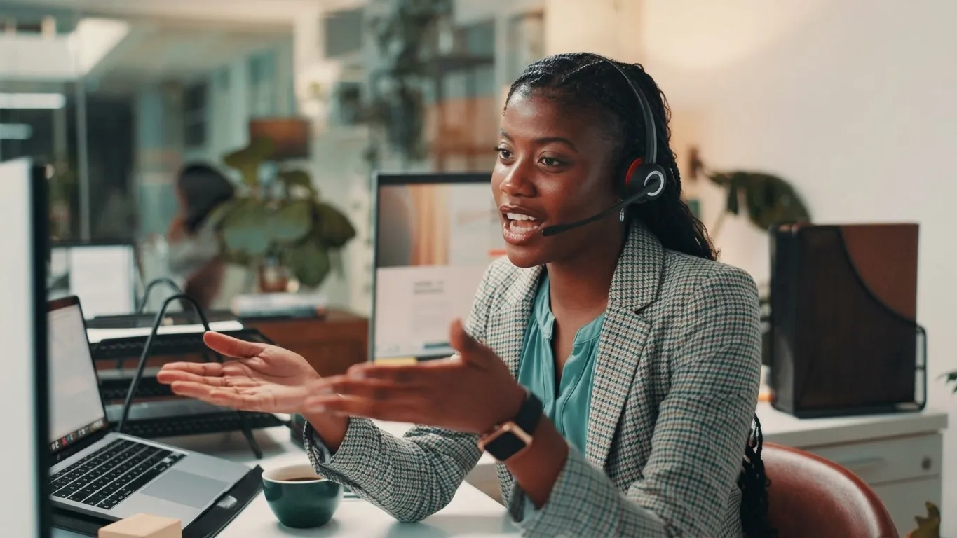 Customer service agent in a headset, gesturing while talking with a caller at a desk