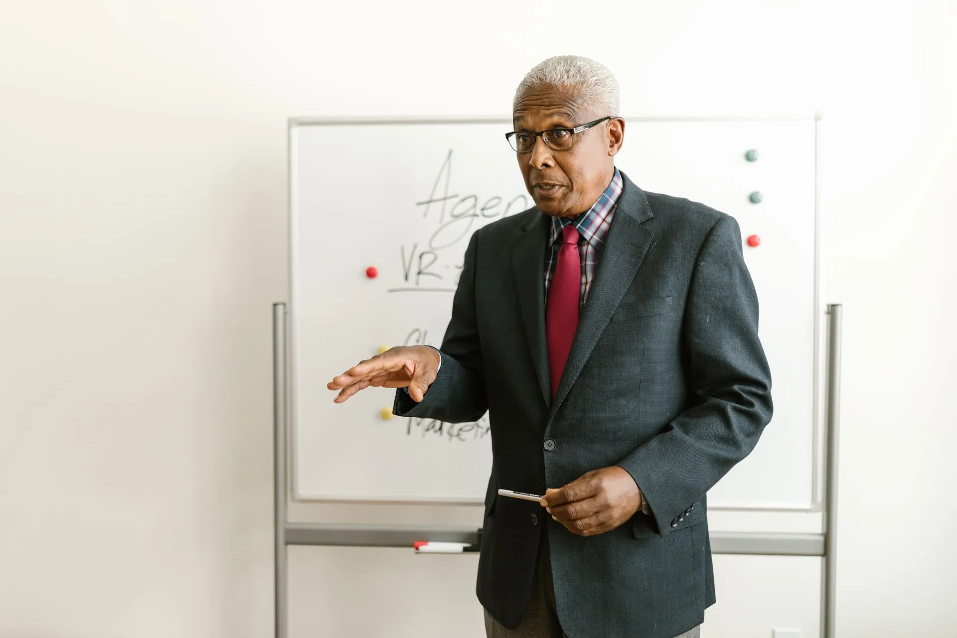 Grey-haired executive in a suit and red tie presenting in front of a whiteboard