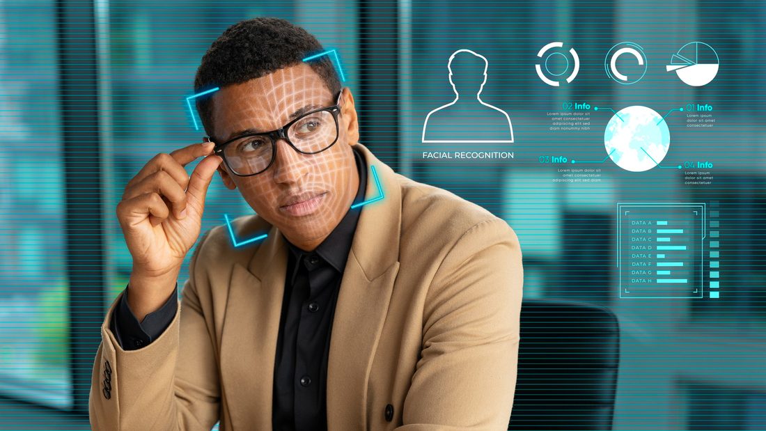 A man in glasses and a tan blazer adjusts his frames while a facial recognition grid is drawn over his face, beside on-screen panels labeled Facial Recognition with a person silhouette, a globe and bar charts